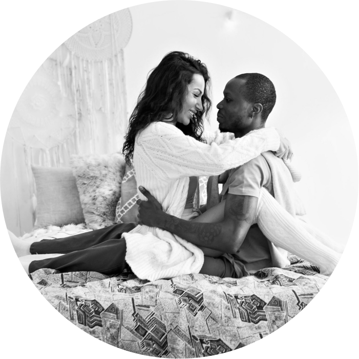 Woman sitting on her partner's lap in bed, embracing him intimately and smiling